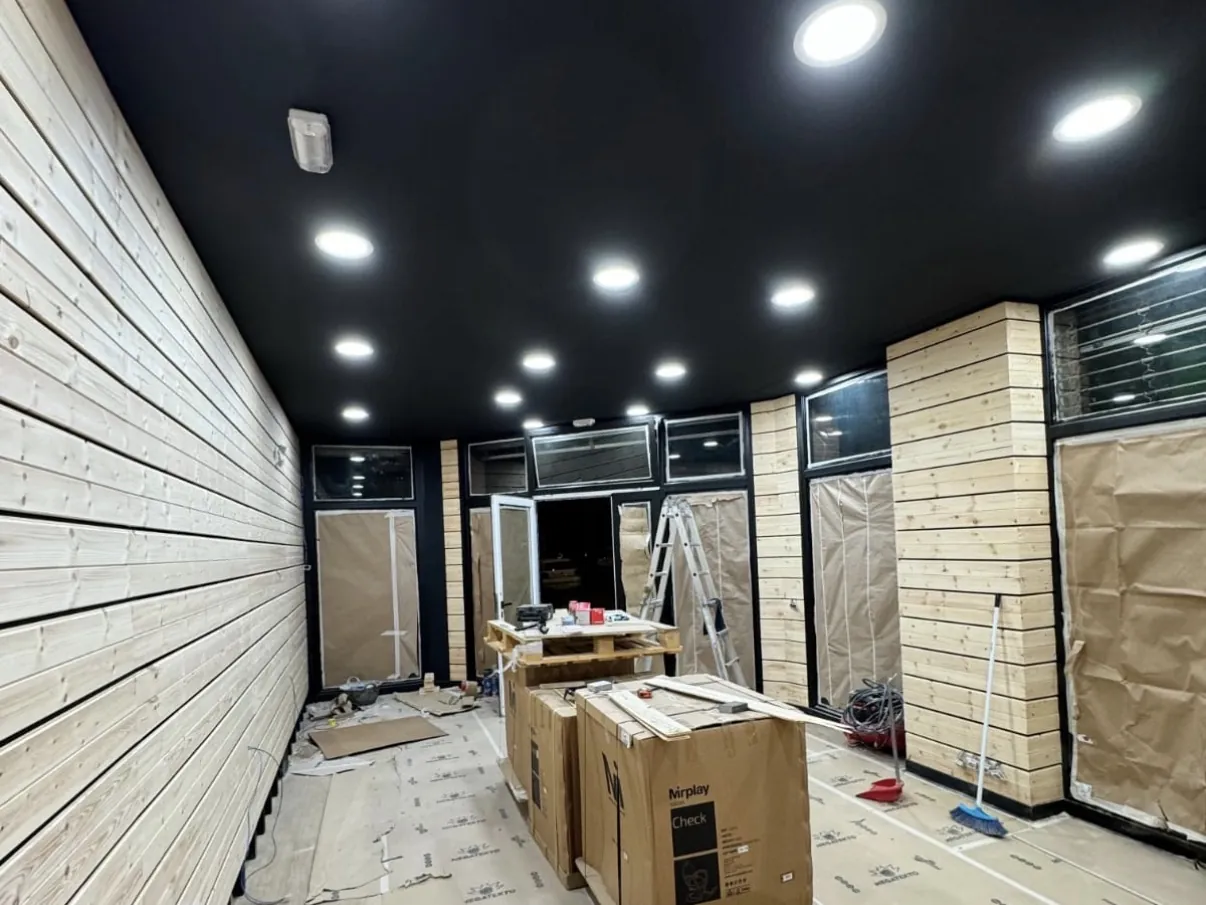 Techo negro con iluminación empotrada y paredes revestidas de madera natural en la barbería de Premià