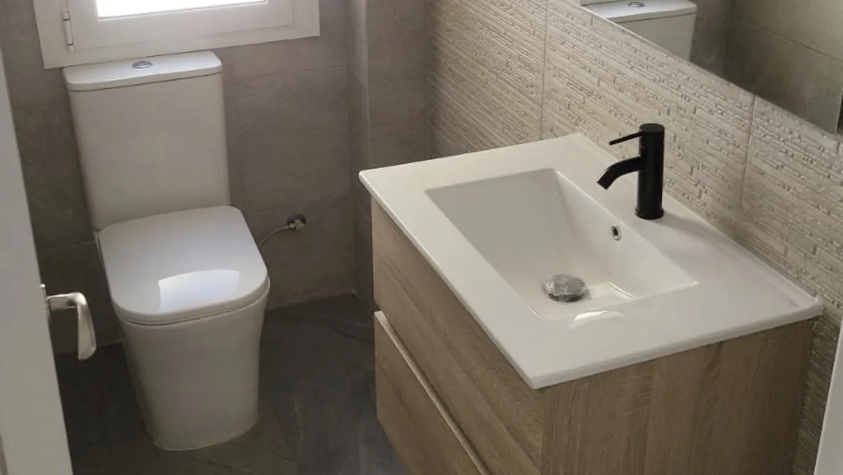 Baño reformado con mueble suspendido de madera, lavabo integrado y grifería negra